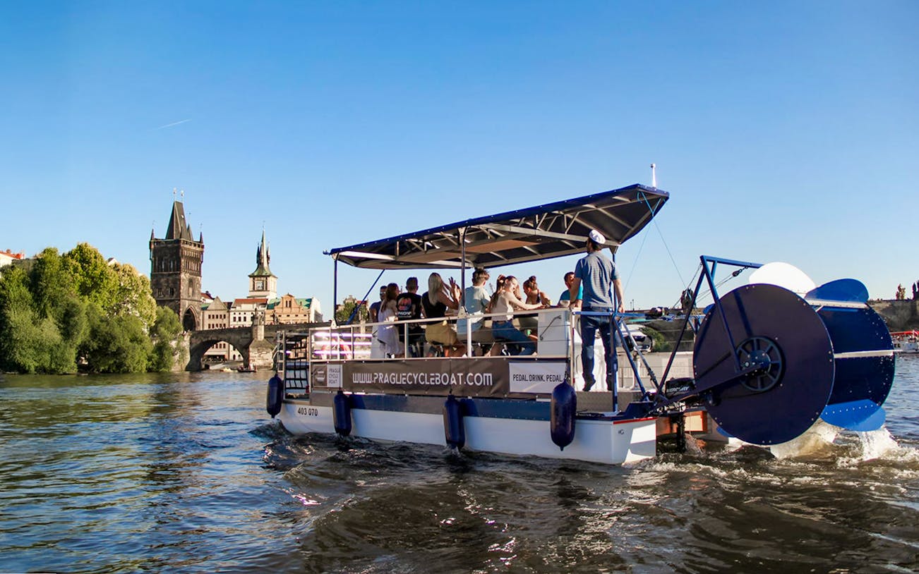 Cycle boat on Vltava River near Charles Bridge, Prague, with passengers enjoying unlimited beer.