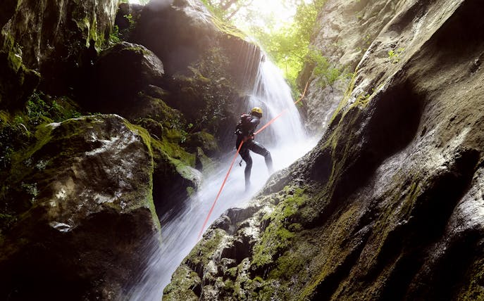 Canyoning adventure at Ribeira dos Caldeirões waterfall with climber descending.
