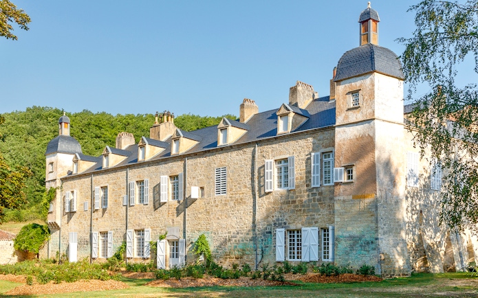 Beaulieu-en-Rouergue Abbey stone building with lush greenery and blue sky.