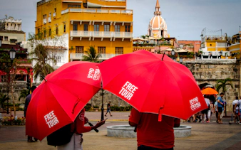 Tourists with red umbrellas in Cartagena's Walled Old City near historic buildings and dome.