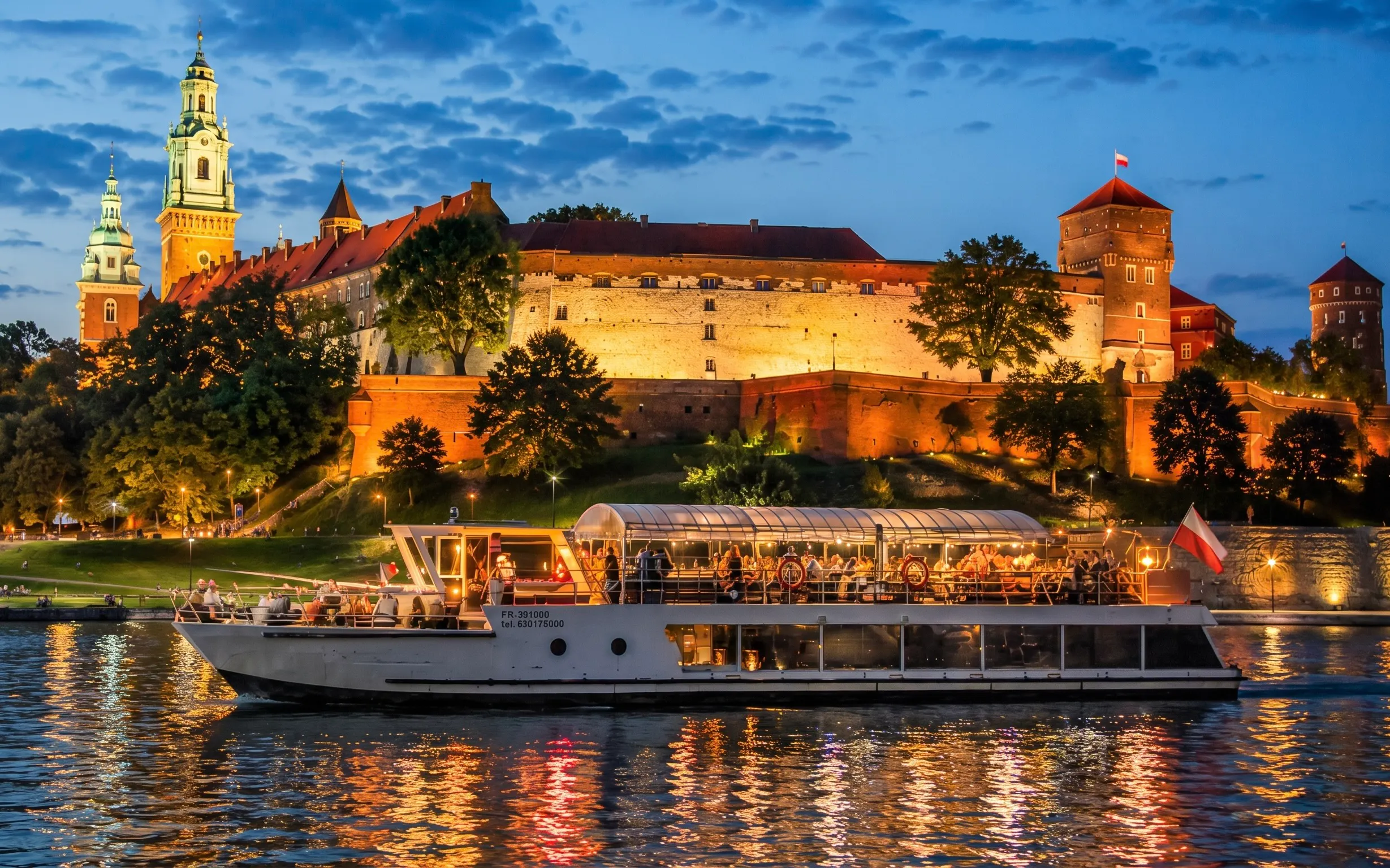 River cruise boat on Vistula River with Wawel Castle illuminated at night in Krakow.