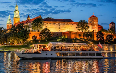 River cruise boat on Vistula River with Wawel Castle illuminated at night in Krakow.