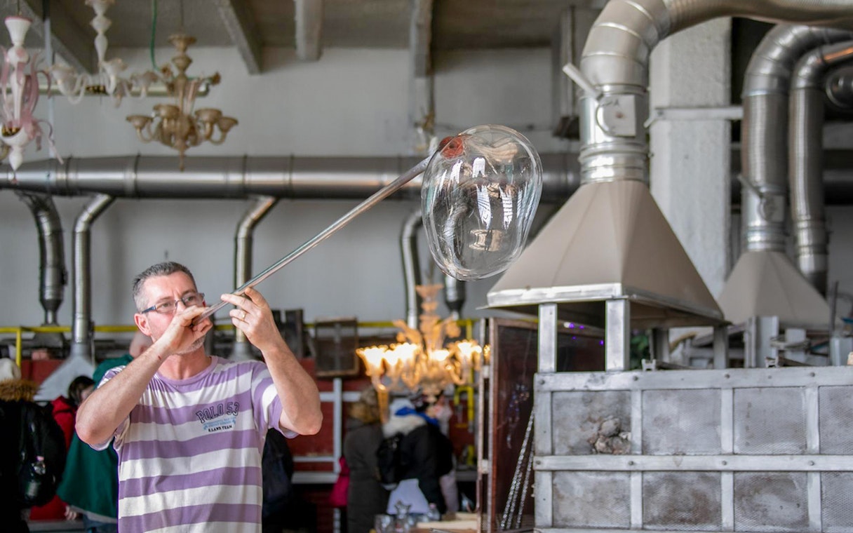 Glassblower shaping molten glass with a blowpipe in a workshop.