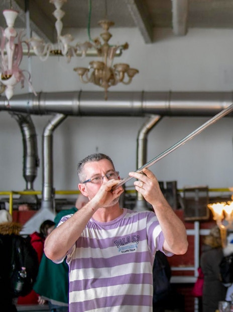Glassblower shaping molten glass with a blowpipe in a workshop.