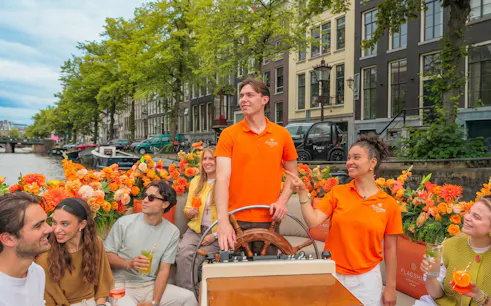 Guests enjoying a canal cruise in Amsterdam with vibrant flowers and historic buildings in the background.