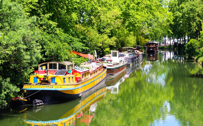 Boats moored along the Canal du Midi in Toulouse, surrounded by lush greenery.