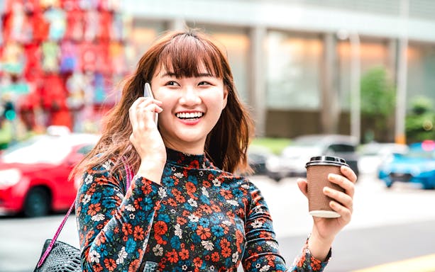 Person using phone with coffee in hand, Singapore street scene.