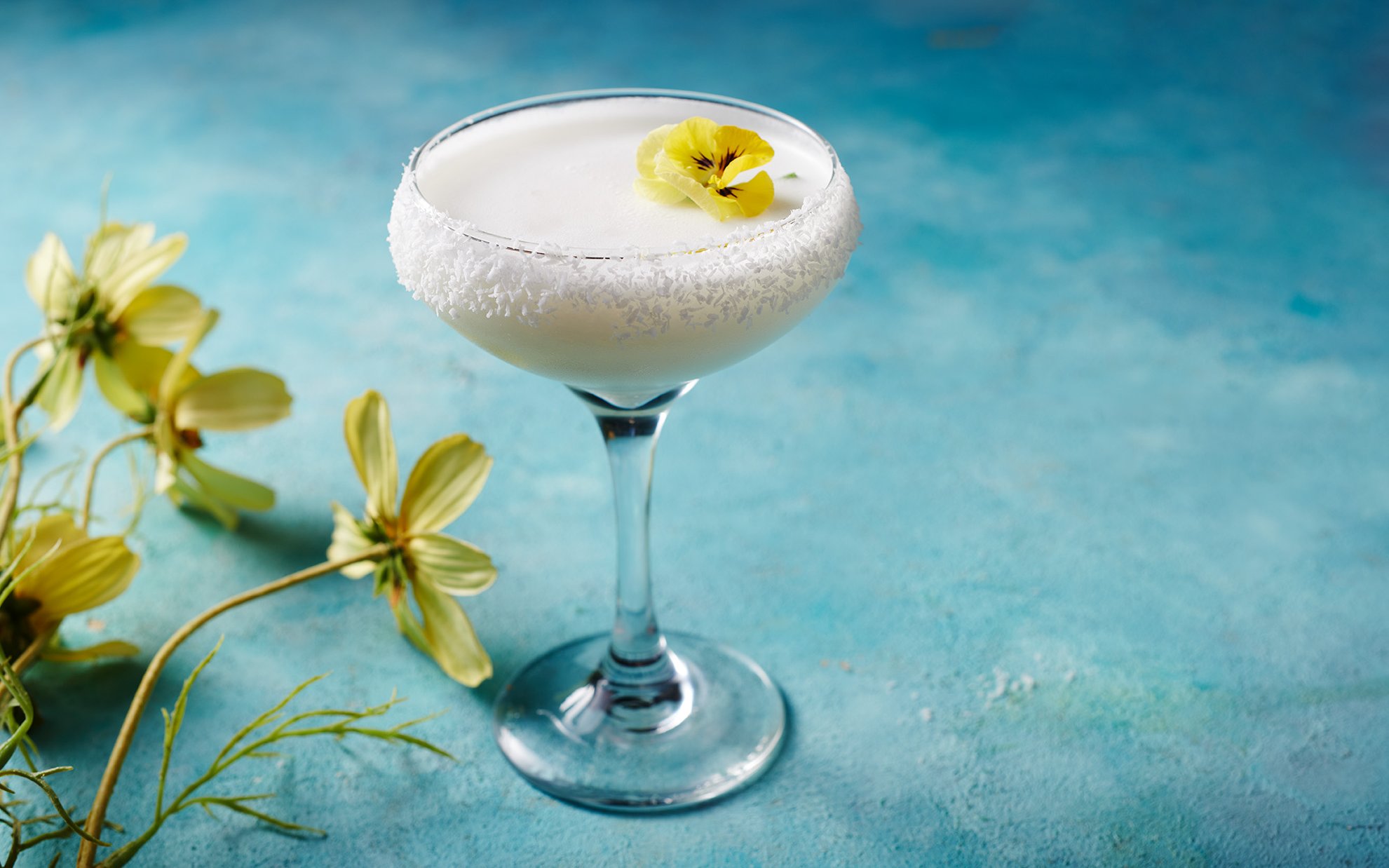 Creamy cocktail with coconut rim and yellow flower garnish at En Fuego Fiesta Mexicana Brunch, Dubai.