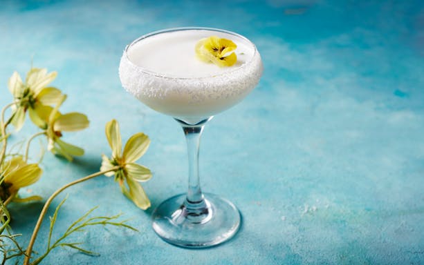 Creamy cocktail with coconut rim and yellow flower garnish at En Fuego Fiesta Mexicana Brunch, Dubai.