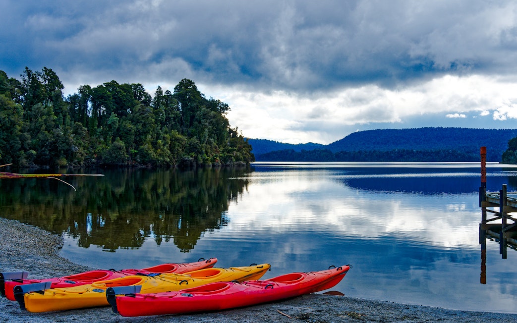 Kayak boats on the shore of Lake Mapourika with forested hills in the background.