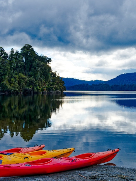 Kayak boats on the shore of Lake Mapourika with forested hills in the background.