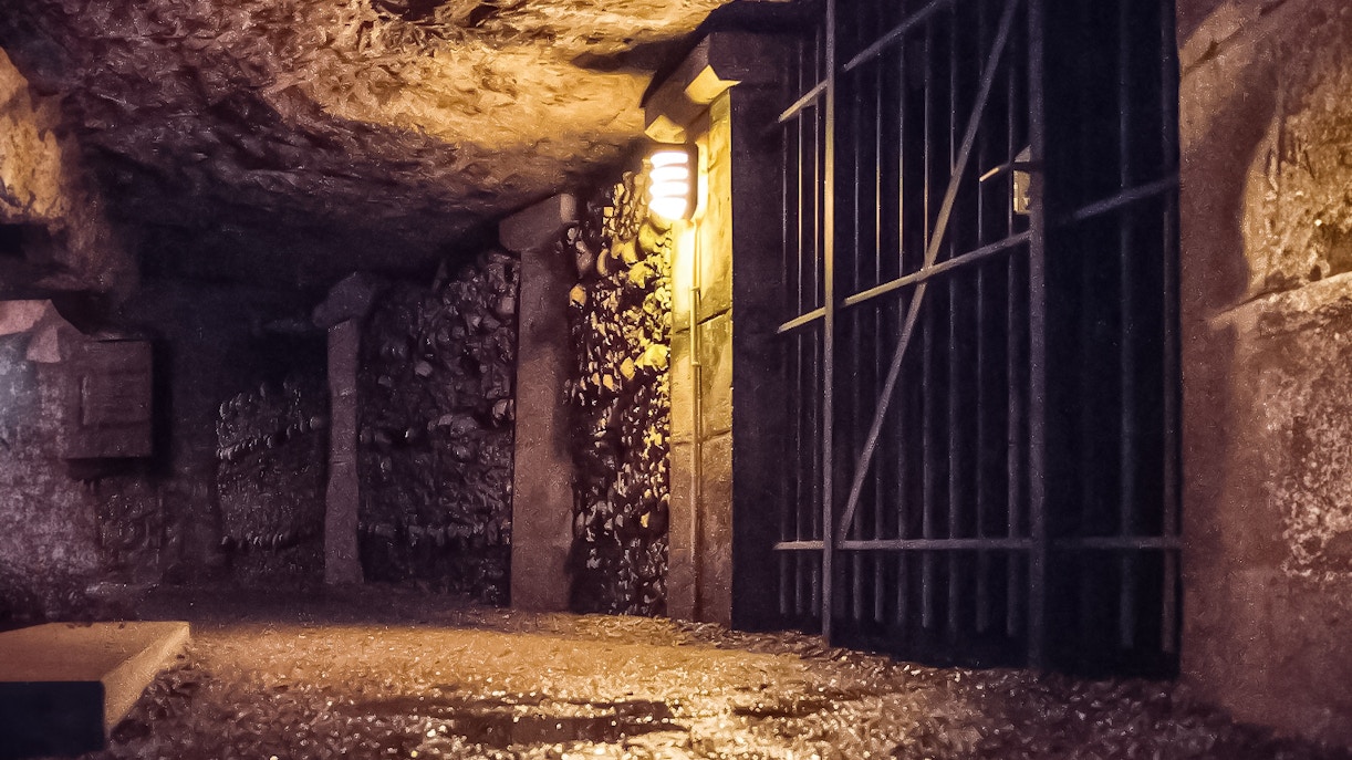 Gate inside Paris Catacombs with illuminated stone walls and metal bars.