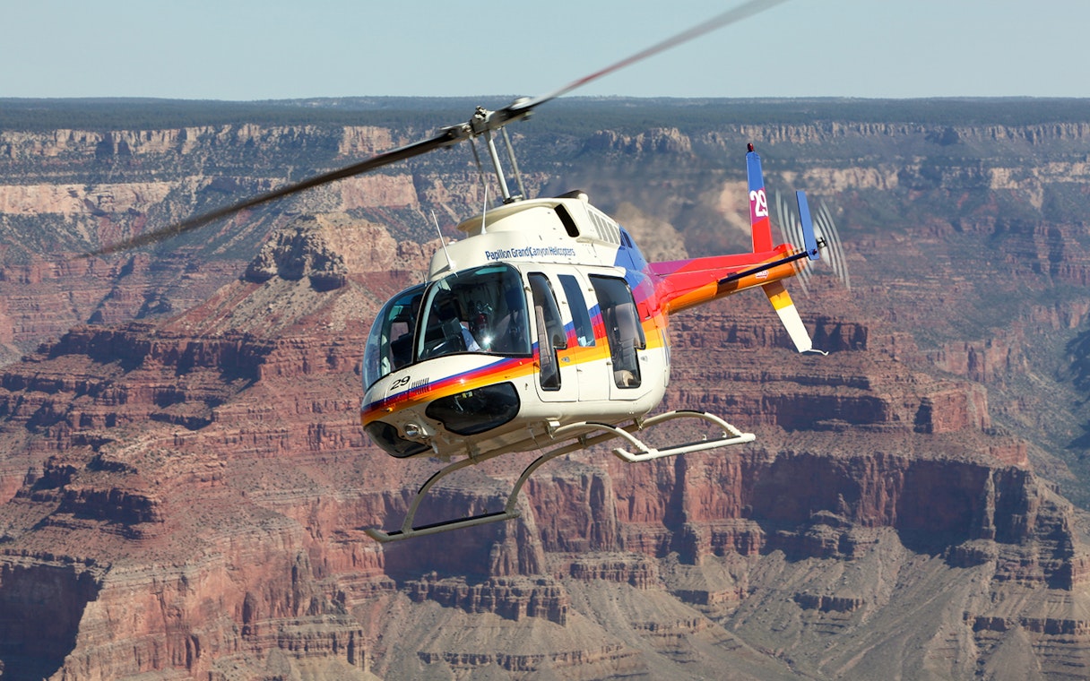 Helicopter flying over the Grand Canyon with rocky cliffs in the background.
