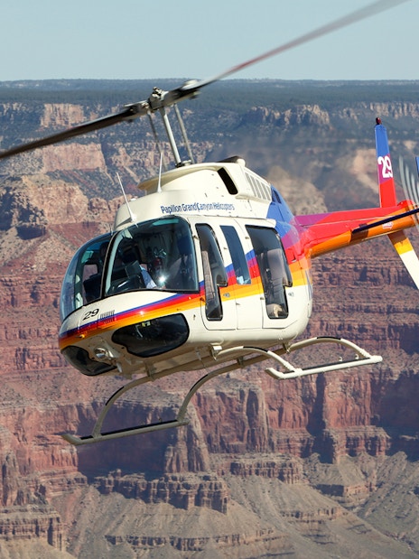 Helicopter flying over the Grand Canyon with rocky cliffs in the background.