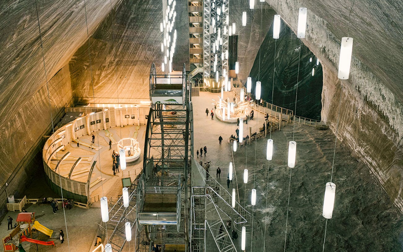 Salina Turda underground salt mine with visitors exploring illuminated caverns.