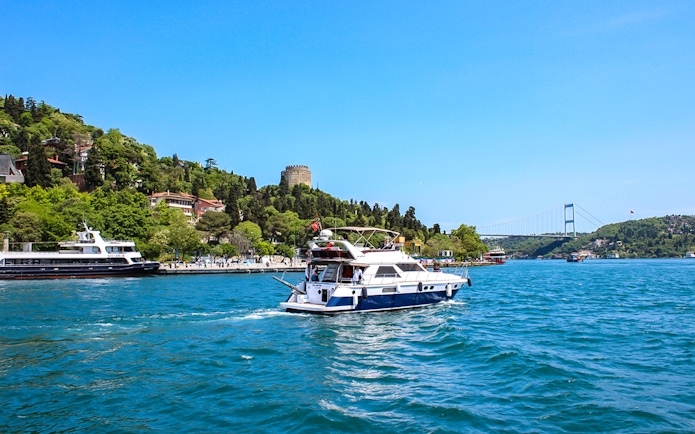 Bosphorus cruise boat near Rumeli Fortress and Bosphorus Bridge in Istanbul.