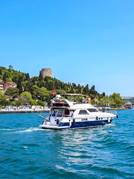 Bosphorus cruise boat near Rumeli Fortress and Bosphorus Bridge in Istanbul.