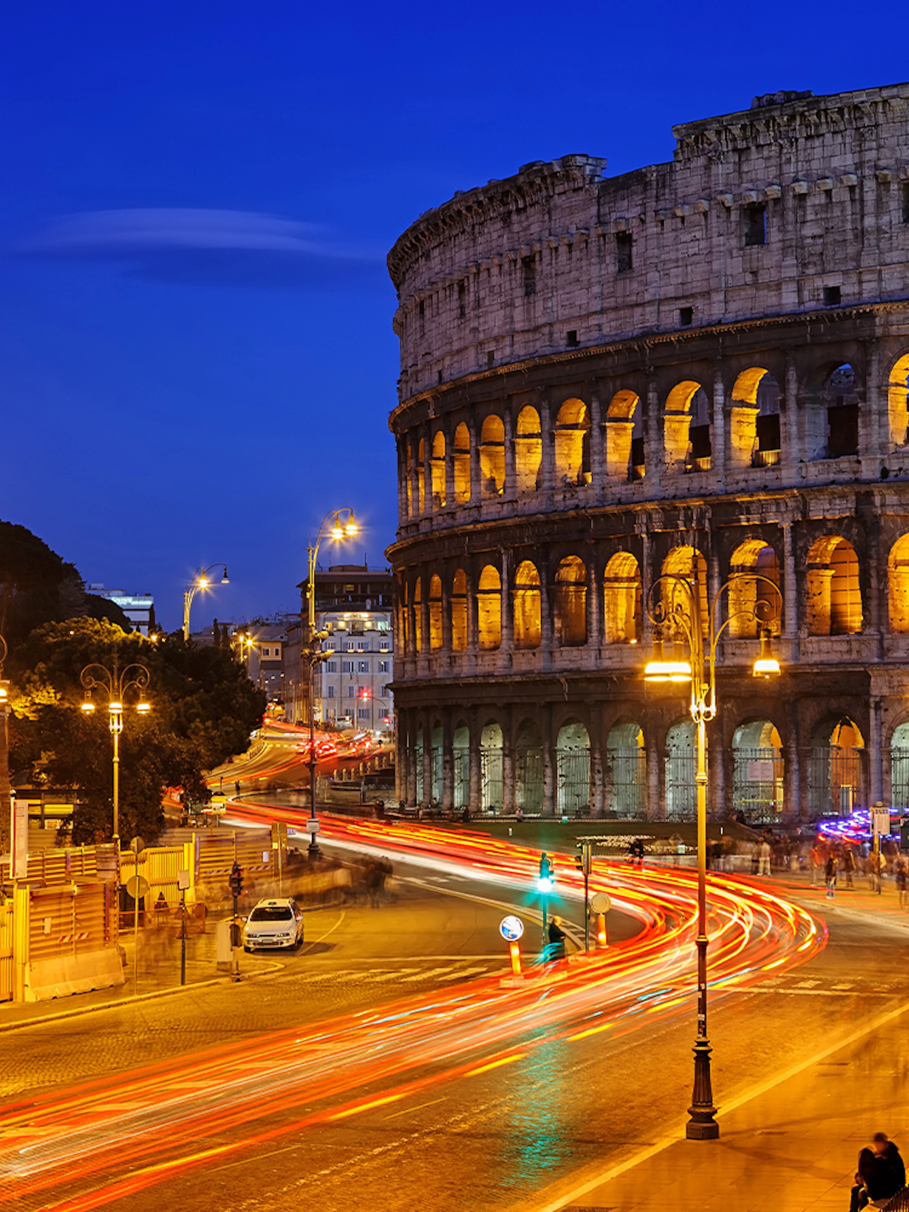 Colosseum illuminated at night with light trails from traffic, Rome HOHO tour.