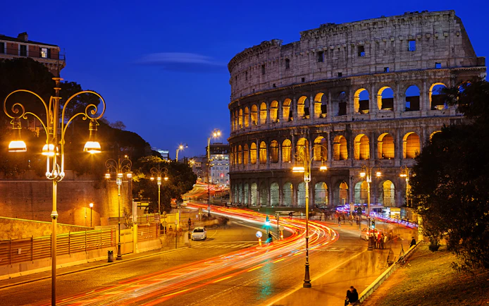 Colosseum illuminated at night with light trails from traffic, Rome HOHO tour.