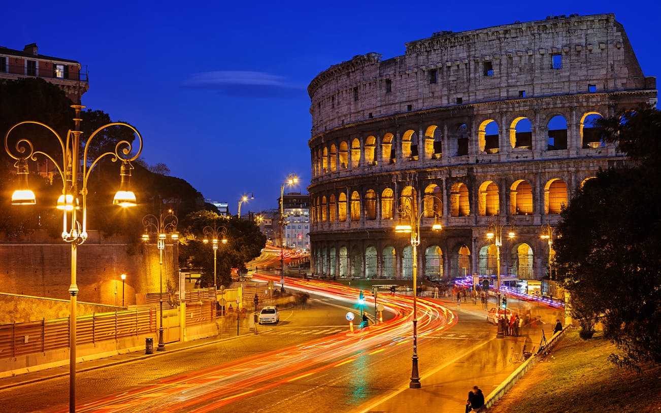 Colosseum illuminated at night with light trails from traffic, Rome HOHO tour.