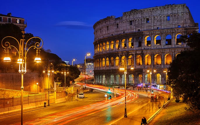 Colosseum illuminated at night with light trails from traffic, Rome HOHO tour.