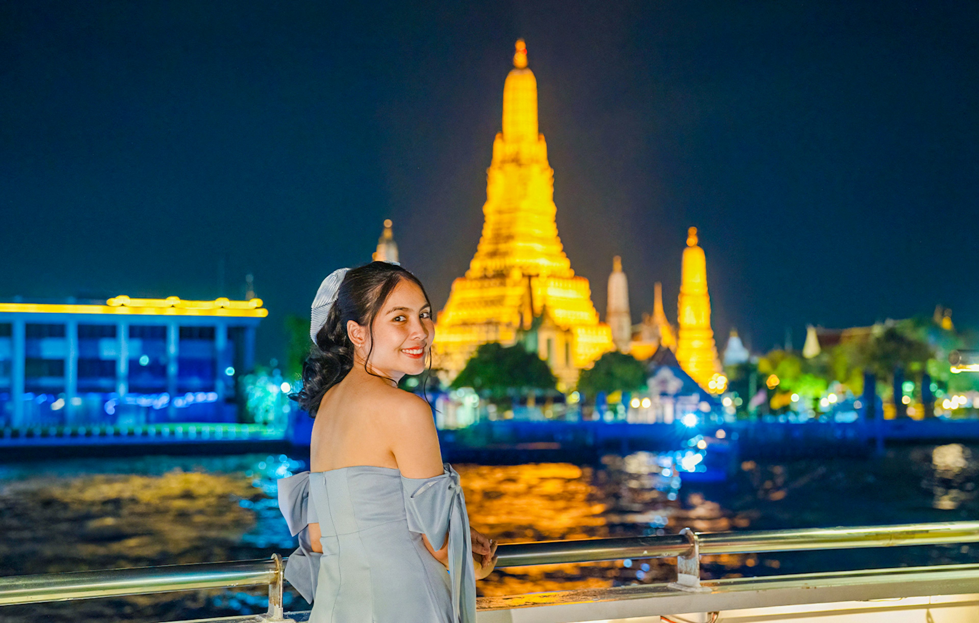 Woman enjoying Smile Riverside Dinner Cruise with Wat Arun illuminated in the background.