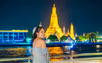 Woman enjoying Smile Riverside Dinner Cruise with Wat Arun illuminated in the background.