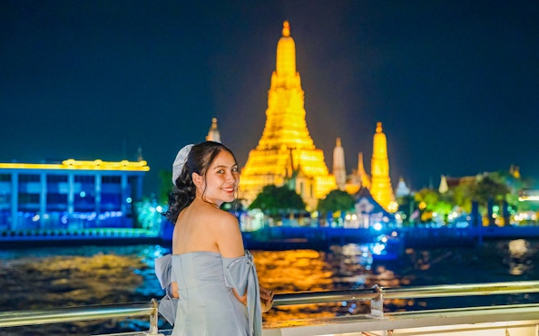 Woman enjoying Smile Riverside Dinner Cruise with Wat Arun illuminated in the background.