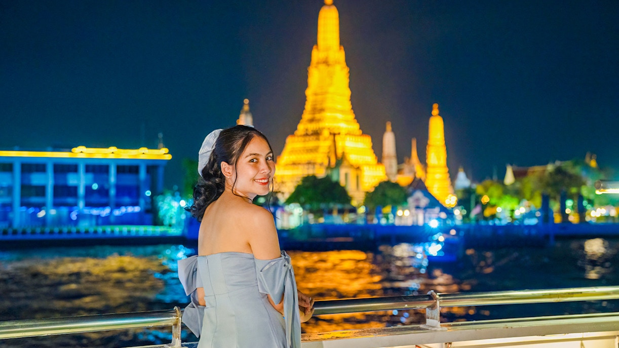Woman enjoying Smile Riverside Dinner Cruise with Wat Arun illuminated in the background.