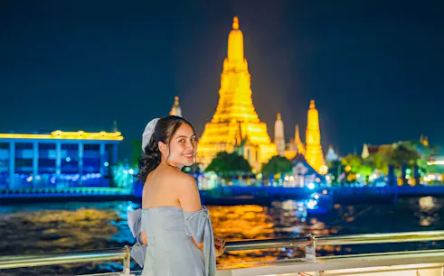 Woman enjoying Smile Riverside Dinner Cruise with Wat Arun illuminated in the background.