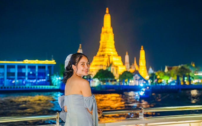 Woman enjoying Smile Riverside Dinner Cruise with Wat Arun illuminated in the background.
