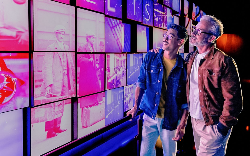 Visitors at Welcome Grid, One World Observatory entrance, New York City skyline images displayed.
