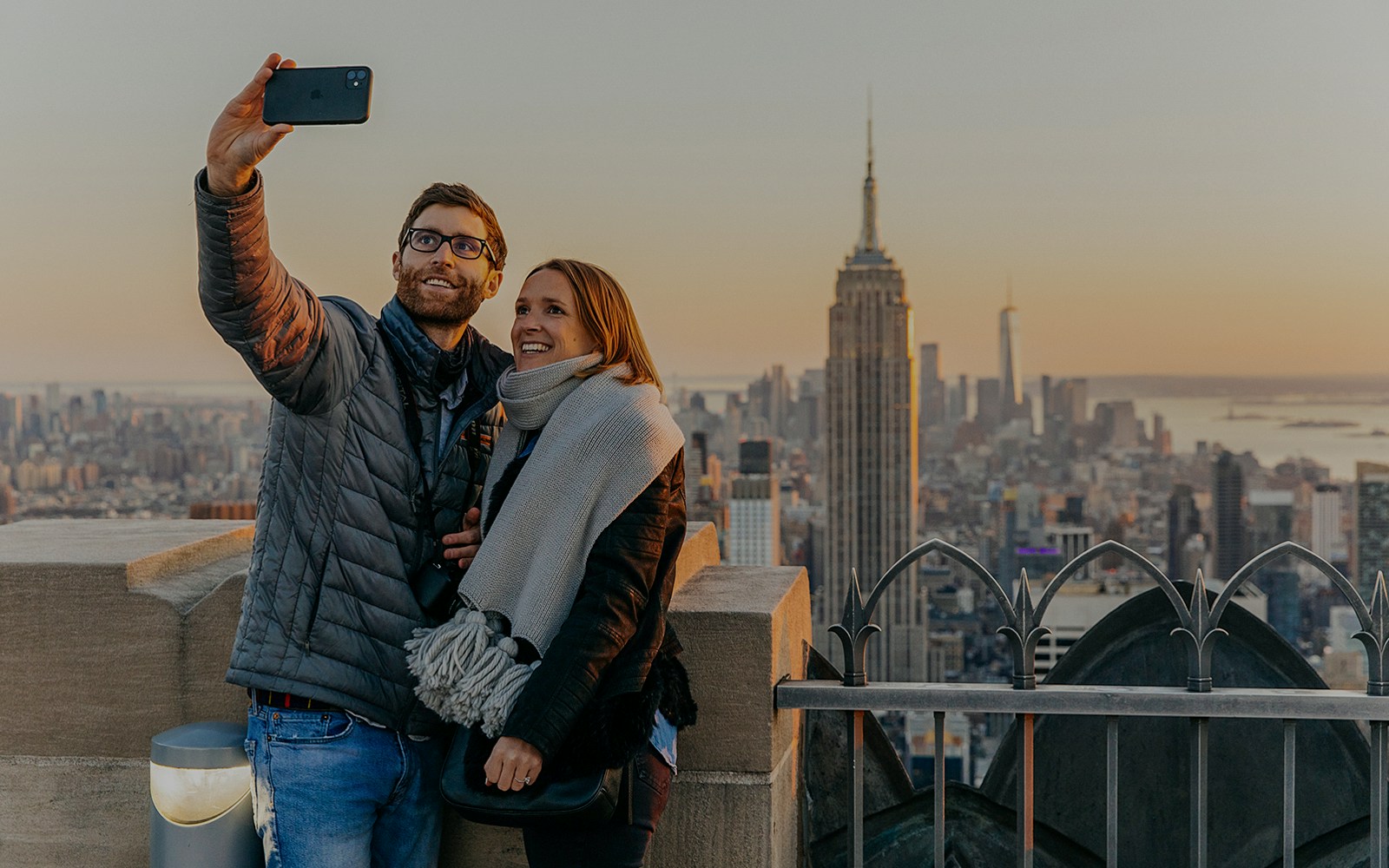 A couple taking a selfie with Empire State building in the background at Top of the Rock, Rockefeller Center, New York