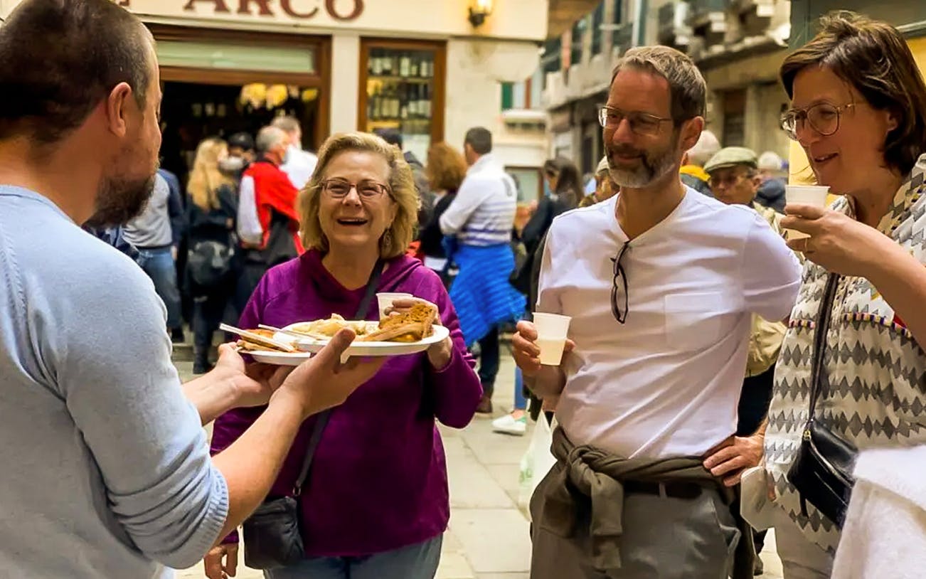 Tourists enjoying street food samples on a guided Venice Rialto Market tour.
