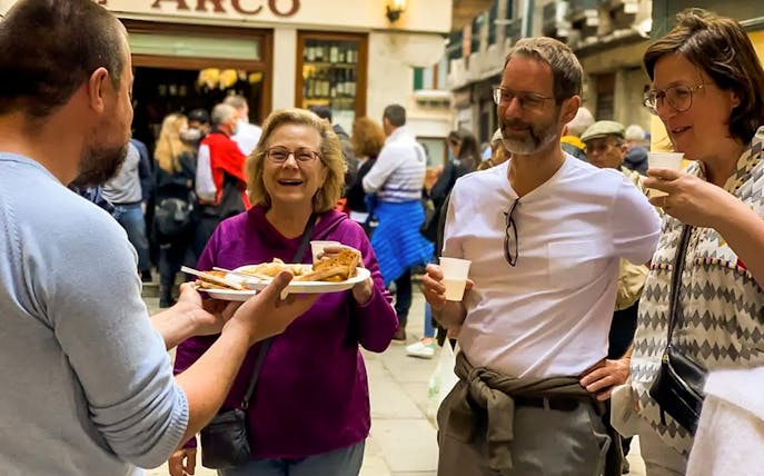 Tourists enjoying street food samples on a guided Venice Rialto Market tour.