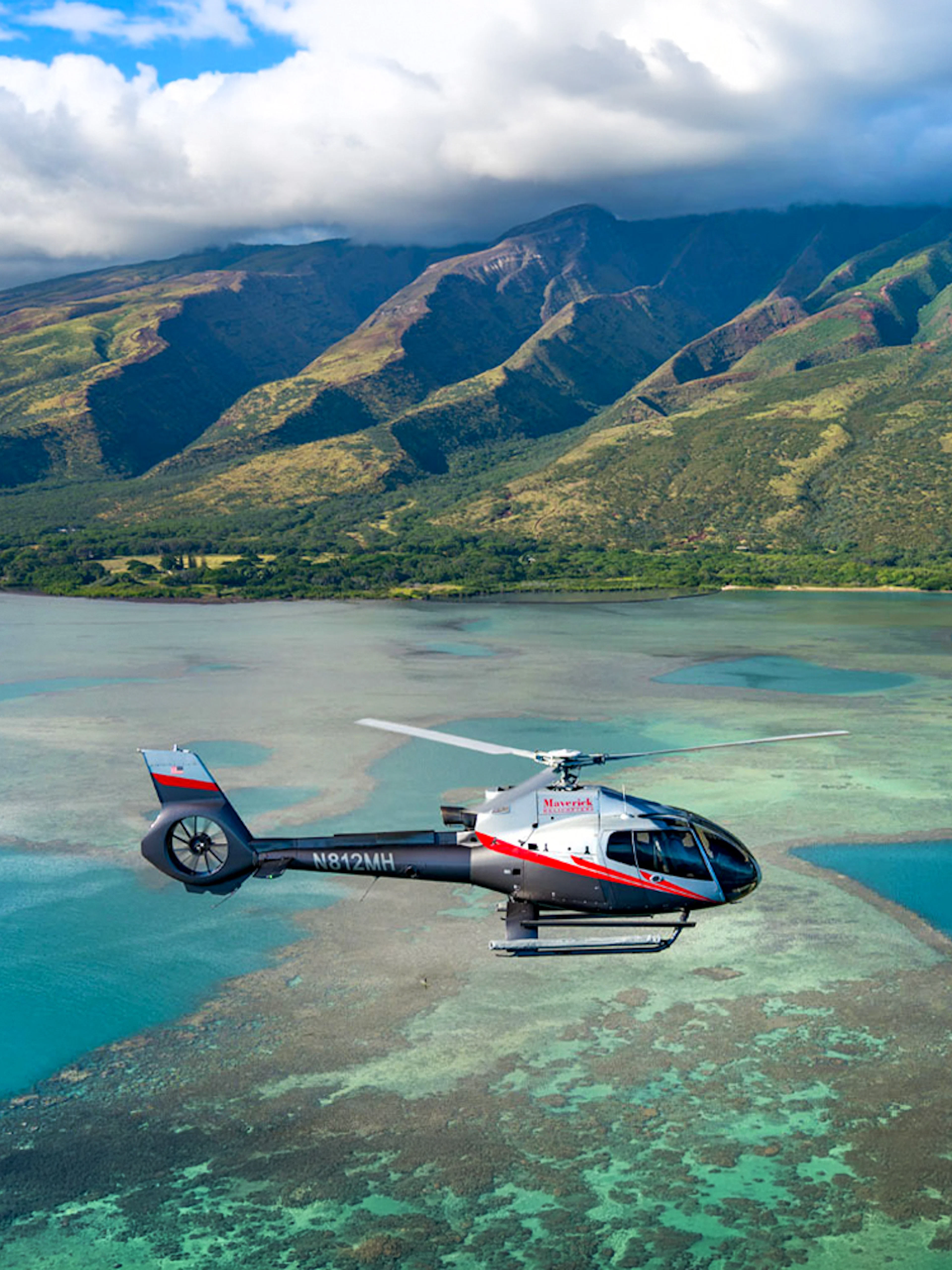 Helicopter flying over Maui's coastline with mountains in the background, Hawaii.
