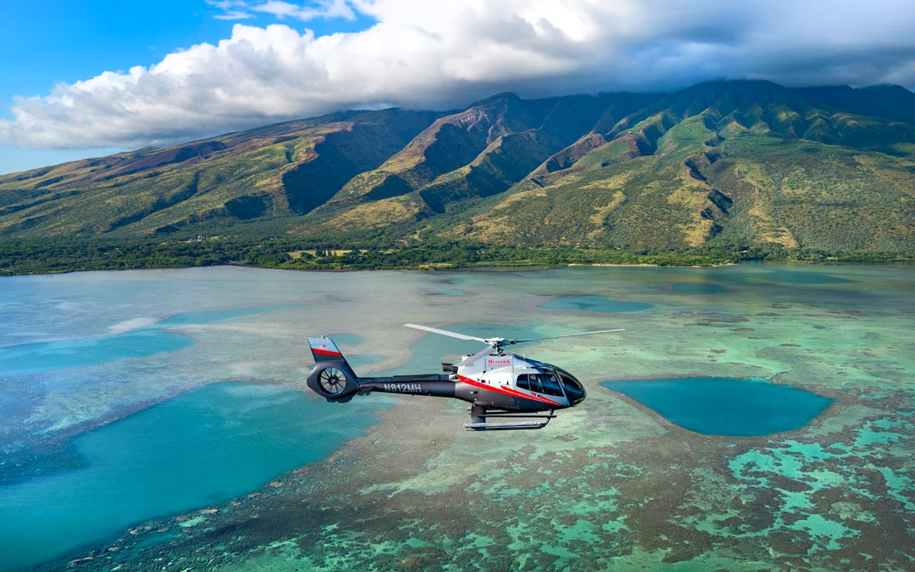 Helicopter flying over Maui's coastline with mountains in the background, Hawaii.