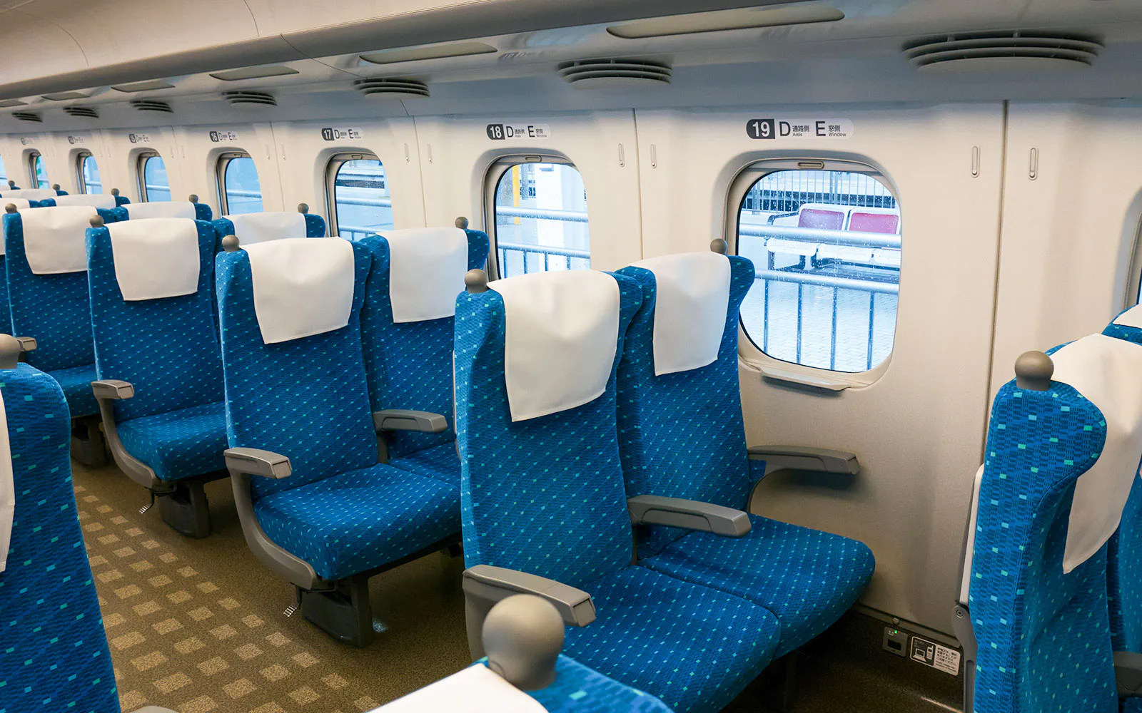 Shinkansen train seats with blue upholstery and white headrests by windows.