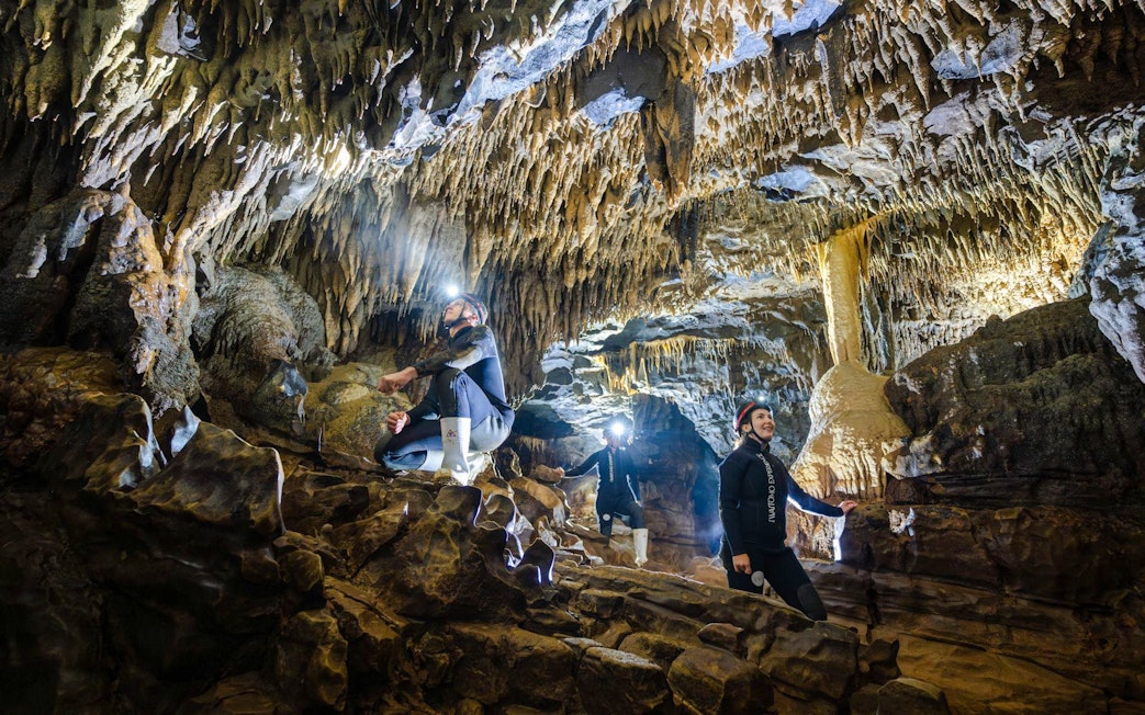 Explorers in Okohua Glowworm Cave, Waitomo, viewing stalactites and rock formations.