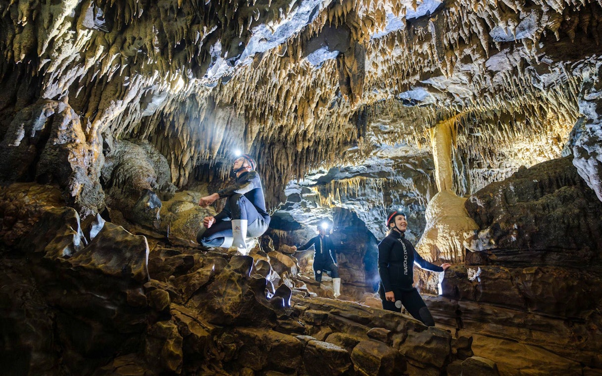 Explorers in Okohua Glowworm Cave, Waitomo, viewing stalactites and rock formations.