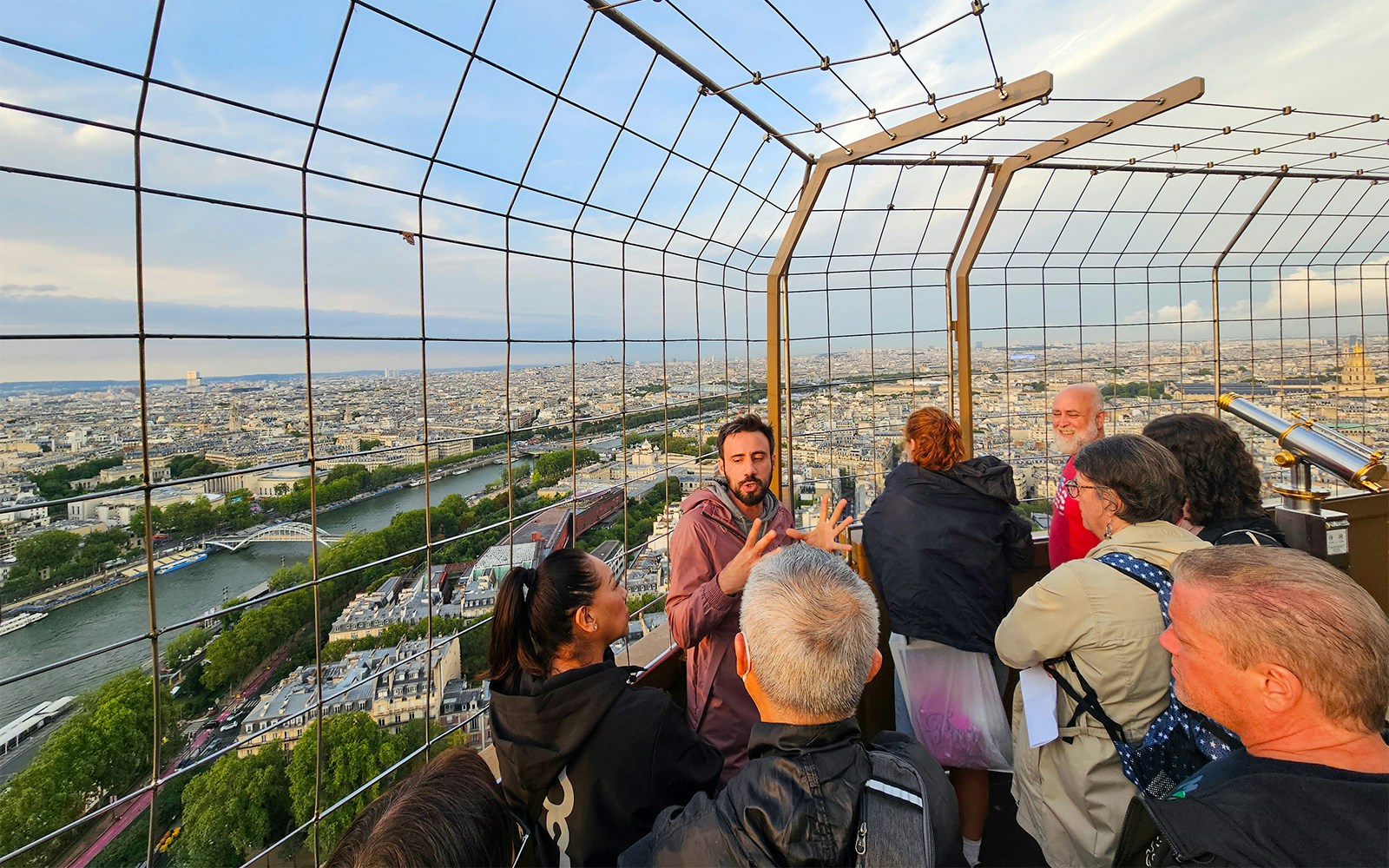 Tourists listening to guide on second floor of Eiffel Tower with Paris skyline.