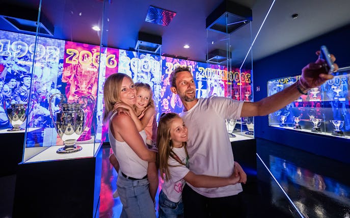 Family taking selfie at FC Barcelona Palau tour with trophy displays in background.