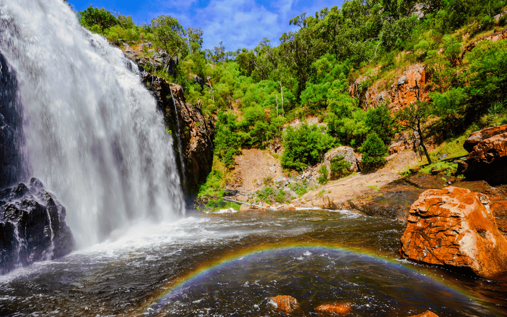 Waterfall cascading over rocks with a rainbow at MacKenzie Falls, surrounded by lush greenery.