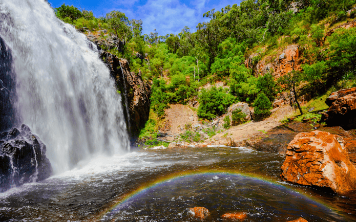 Waterfall cascading over rocks with a rainbow at MacKenzie Falls, surrounded by lush greenery.