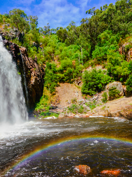 Waterfall cascading over rocks with a rainbow at MacKenzie Falls, surrounded by lush greenery.