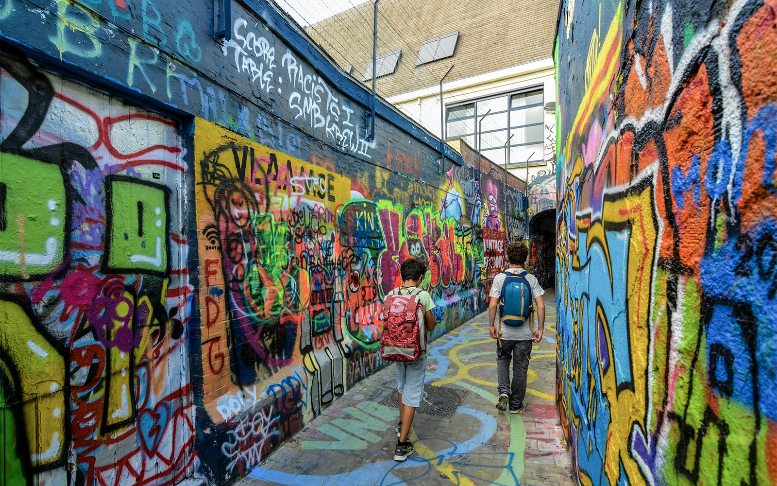Graffiti-covered alley with two people walking, Ghent, Belgium.