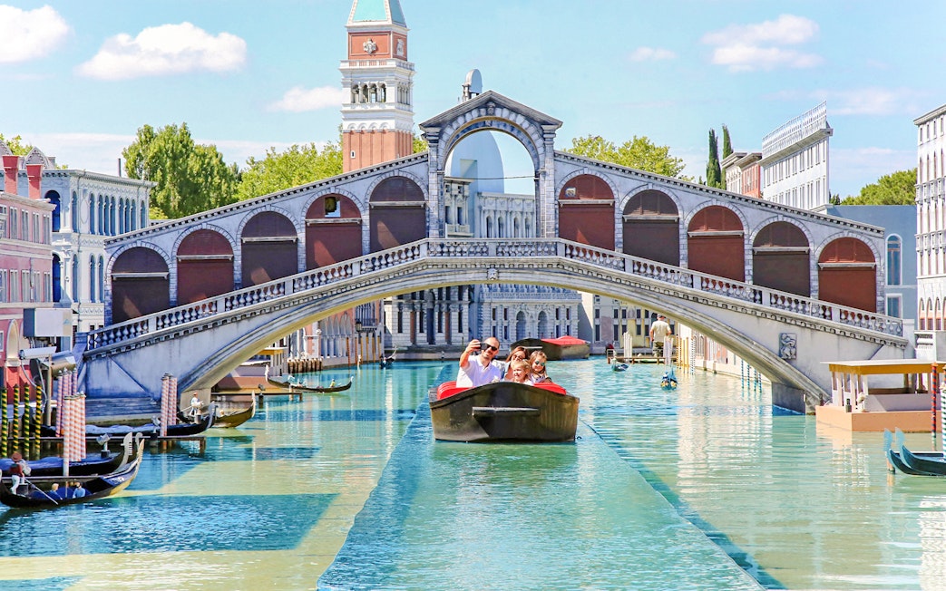 Family on a boat under a miniature Rialto Bridge at Italia in Miniatura, Italy.