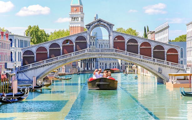 Family on a boat under a miniature Rialto Bridge at Italia in Miniatura, Italy.