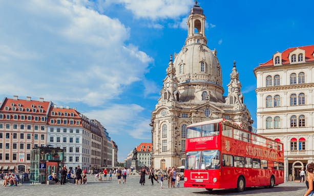 Red double-decker bus in front of Dresden's Frauenkirche during a city tour.
