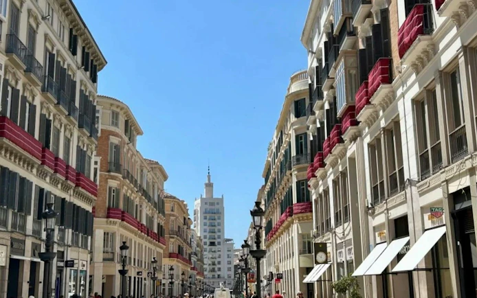 Street view of historic buildings in Málaga with red awnings and a distant tower.